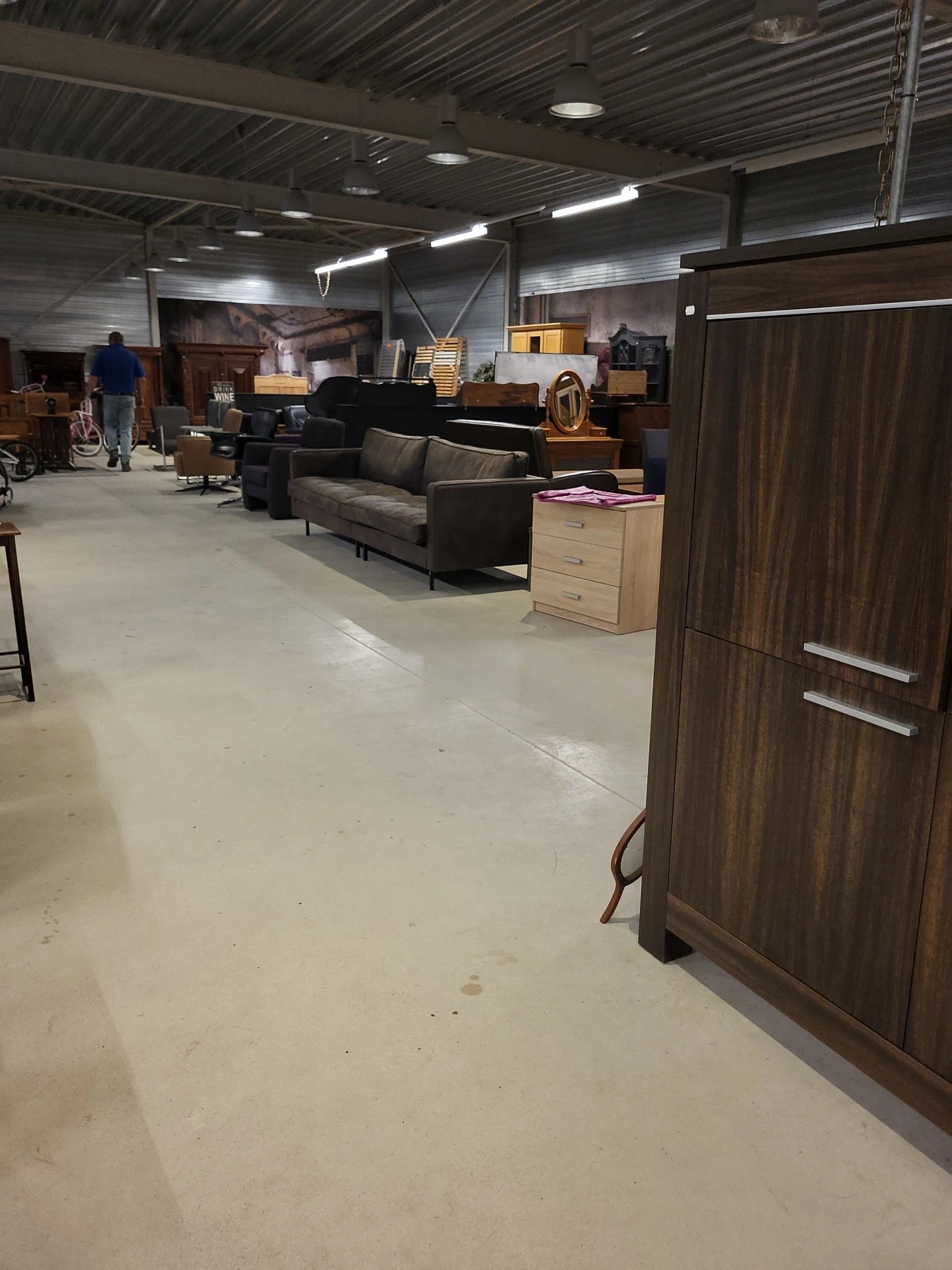 Winkelvloer met uitgestalde meubels: grijze bank, houten kasten en ander meubilair in kringloopwinkel