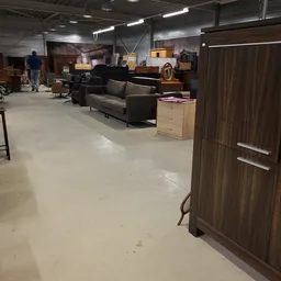 Winkelvloer met uitgestalde meubels: grijze bank, houten kasten en ander meubilair in kringloopwinkel