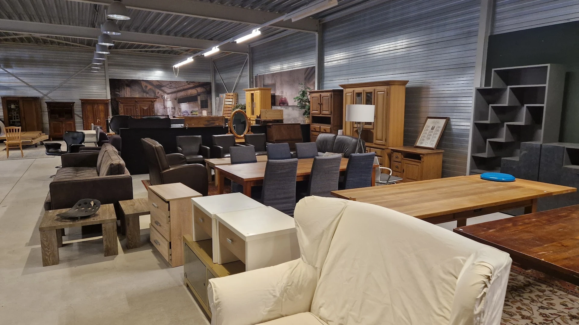 Winkelvloer met uitgestalde meubels: eetkamerstoelen, tafels, kasten en een crèmekleurige zithoek onder industriële verlichti
