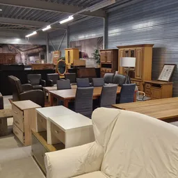 Winkelvloer met uitgestalde meubels: eetkamerstoelen, tafels, kasten en een crèmekleurige zithoek onder industriële verlichti