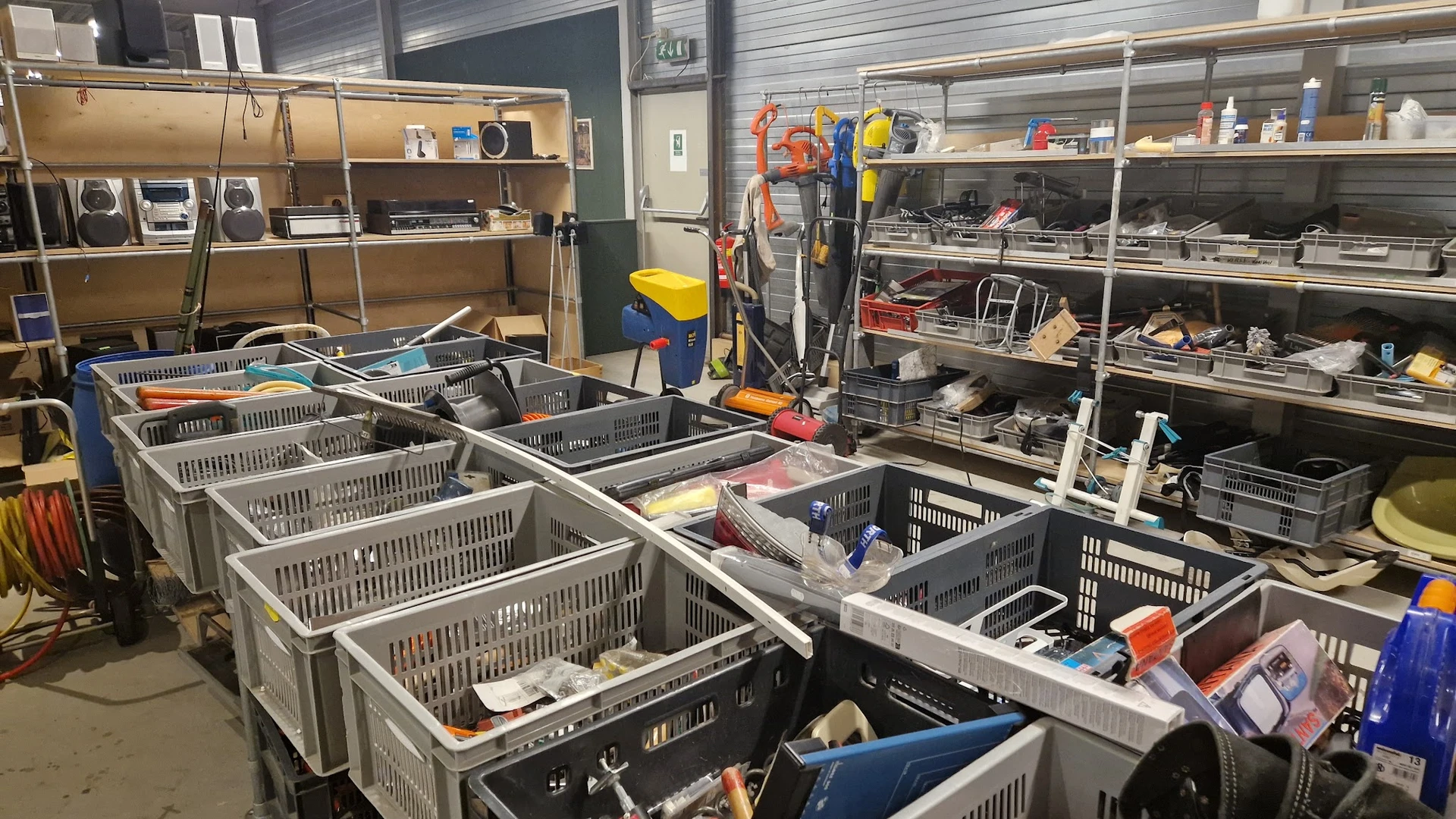 Plastic kratten en bakken met diverse spullen op tafels in een kringloopwinkel
