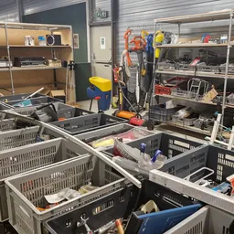 Plastic kratten en bakken met diverse spullen op tafels in een kringloopwinkel