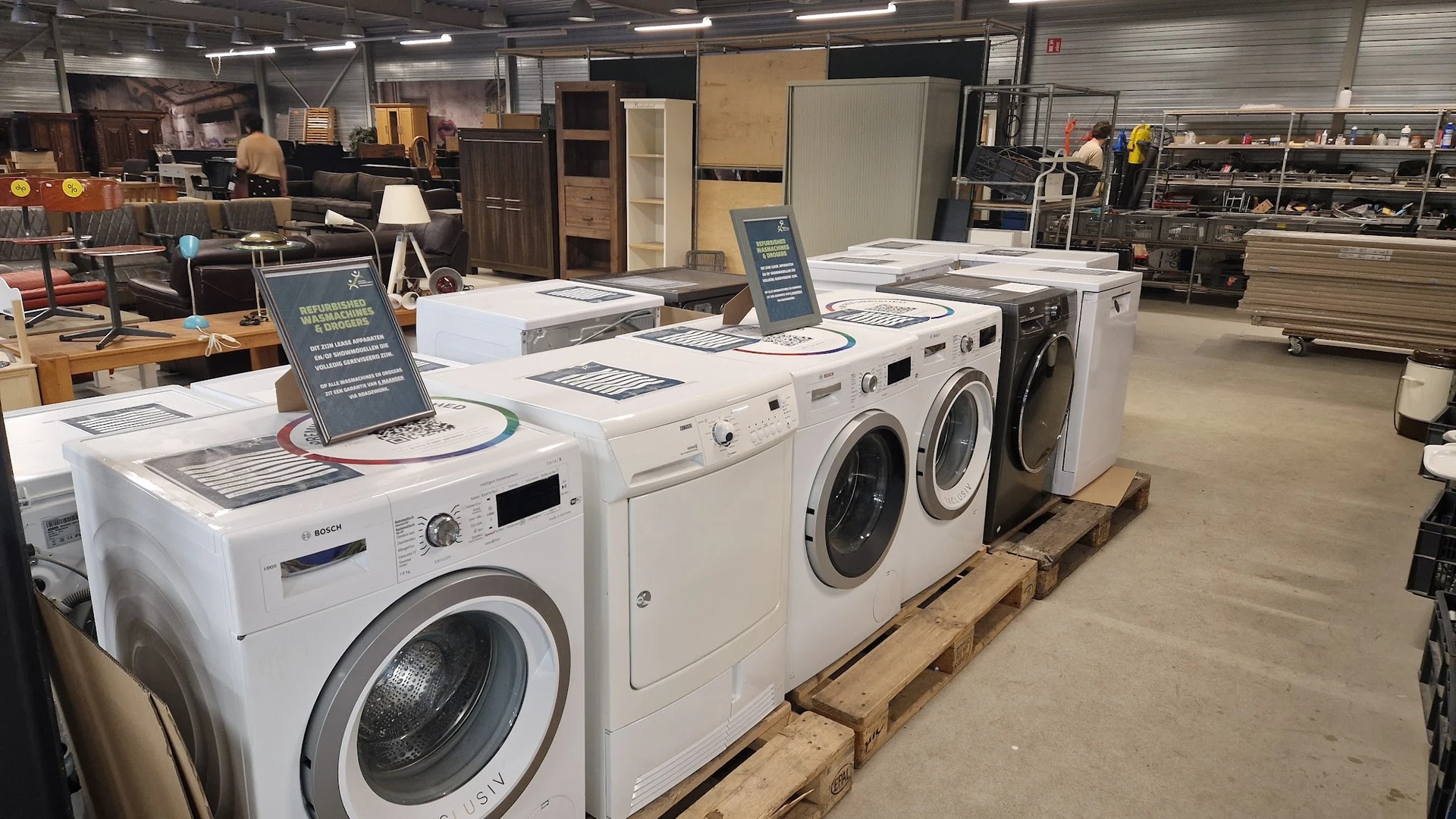 Uitgestalde wasmachines en droogkasten in wit en zwart op houten pallets in de winkel