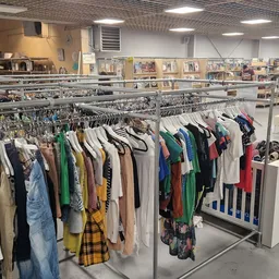 Rekken met tweedehands kleding op hangers in kringloopwinkel, op achtergrond boeken in kasten