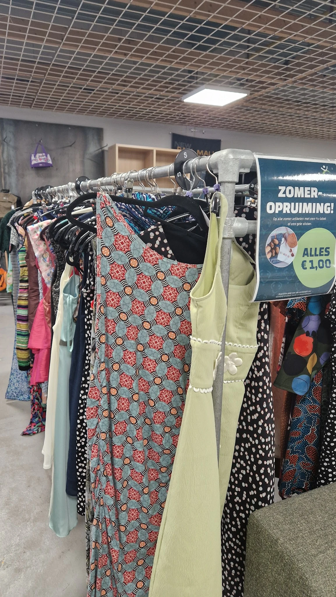 Rekken met tweedehands kleding in verschillende kleuren en patronen, met opvallend een jurk met rood-wit-groen bloemenpatroon