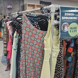 Rekken met tweedehands kleding in verschillende kleuren en patronen, met opvallend een jurk met rood-wit-groen bloemenpatroon