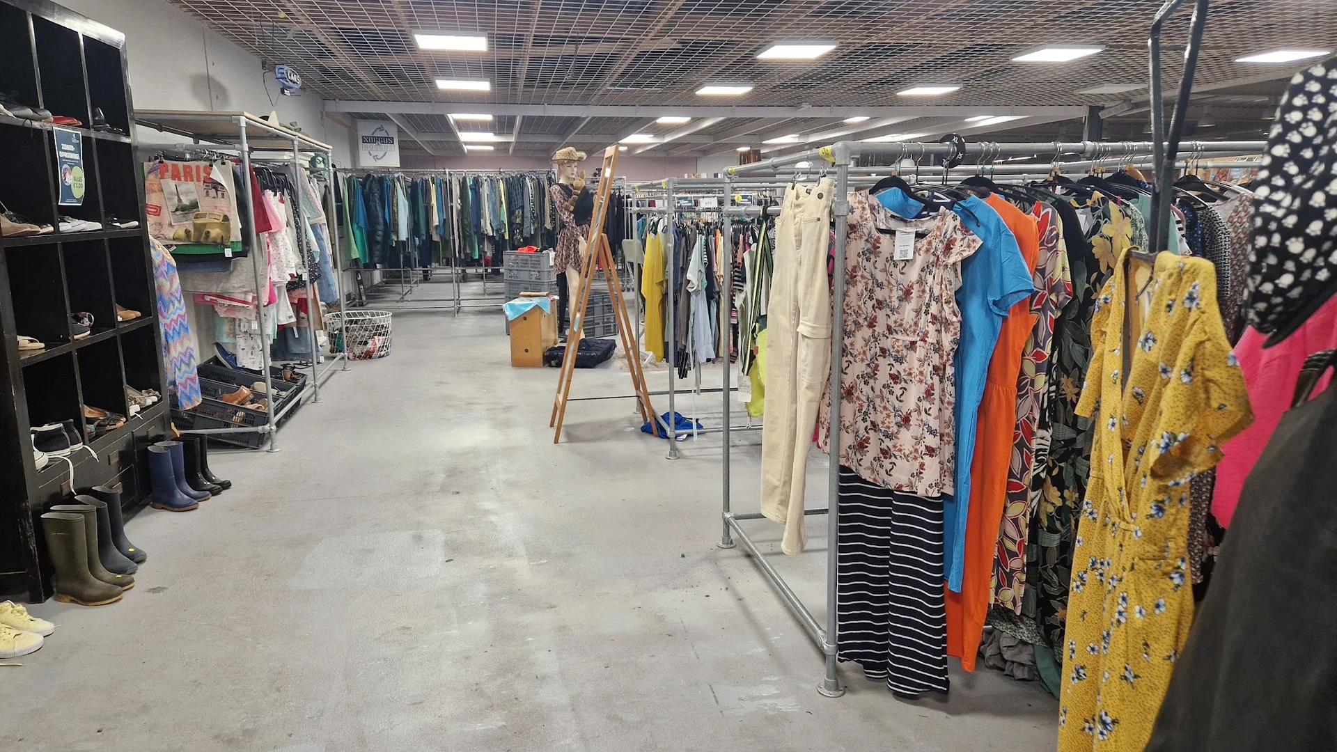 Winkelvloer met kledingrekken vol tweedehands kleding in verschillende kleuren en patronen