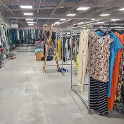 Winkelvloer met kledingrekken vol tweedehands kleding in verschillende kleuren en patronen