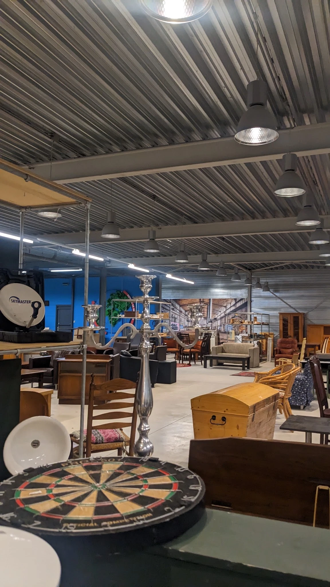 Ruim magazijn met diverse tweedehands meubels, stoelen, kasten en huisraad uitgestald onder LED-verlichting