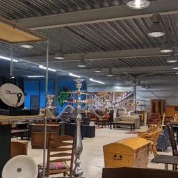 Ruim magazijn met diverse tweedehands meubels, stoelen, kasten en huisraad uitgestald onder LED-verlichting