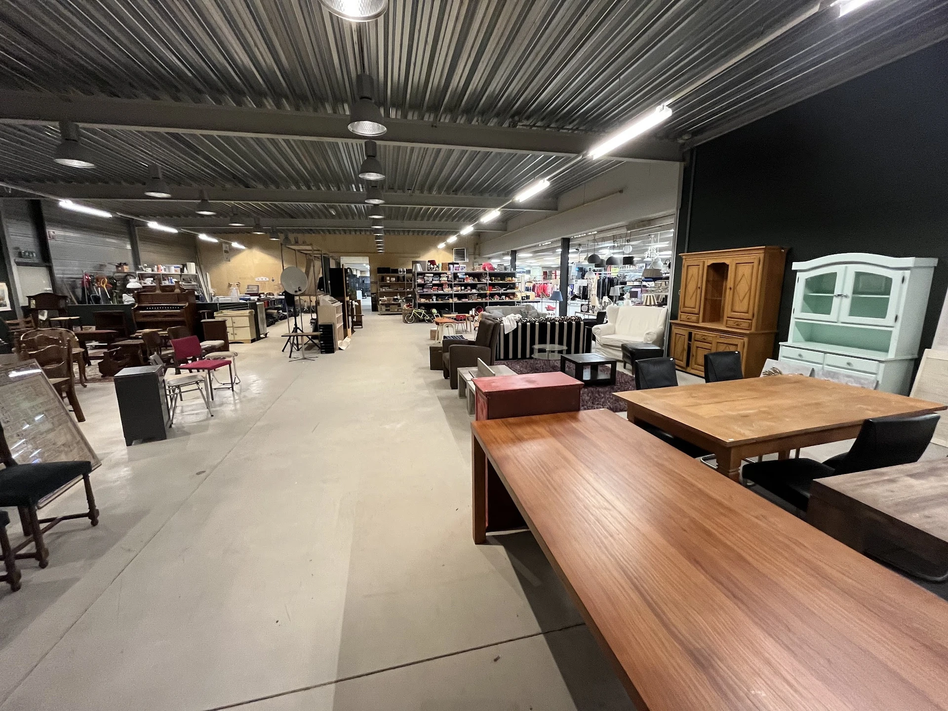 Ruim winkelinterieur met houten meubels, tafels en diverse tweedehandsartikelen uitgestald