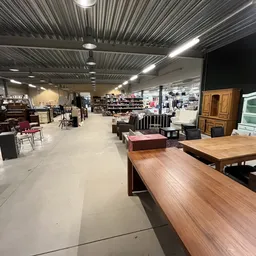 Ruim winkelinterieur met houten meubels, tafels en diverse tweedehandsartikelen uitgestald