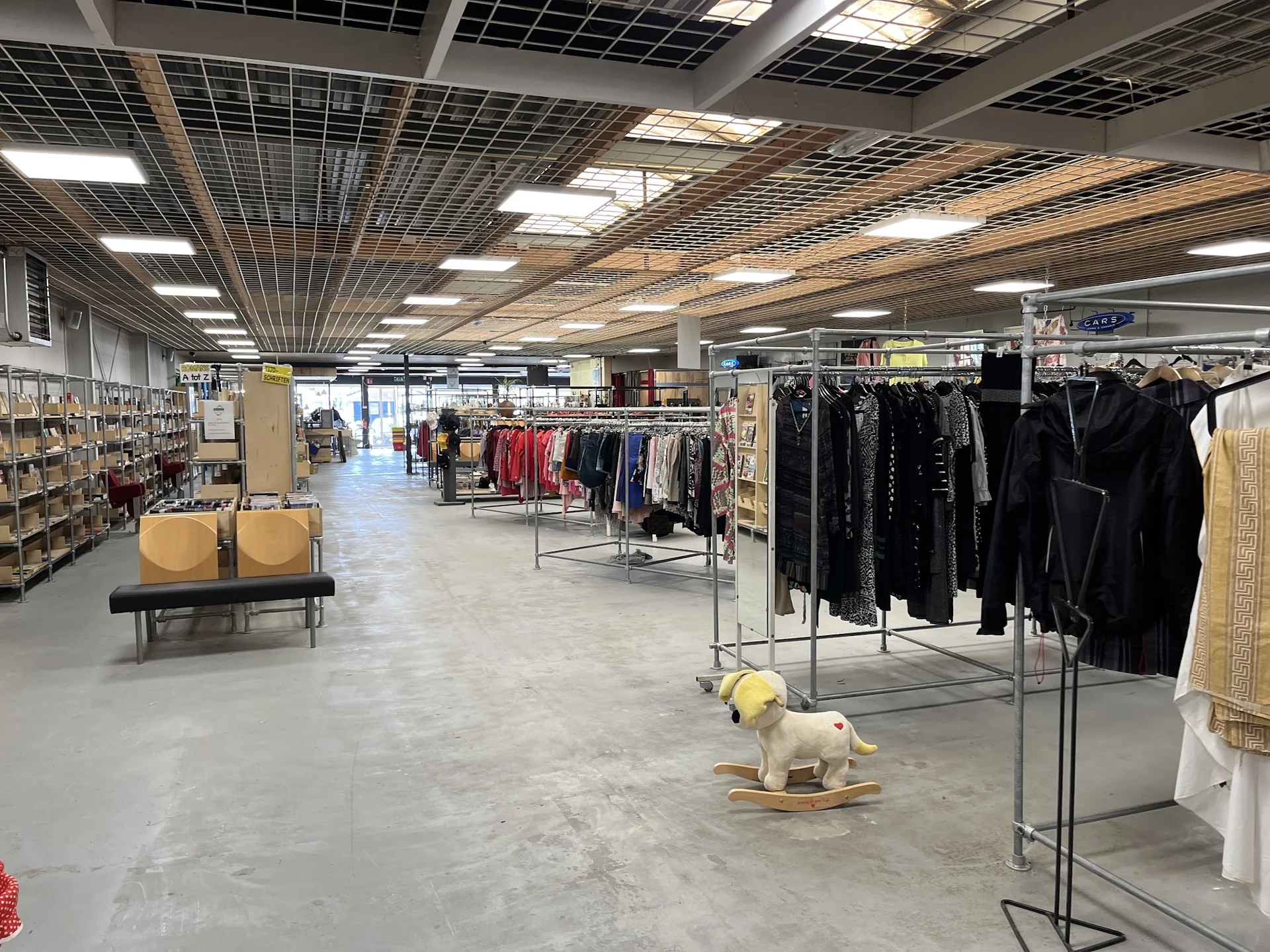 Winkelvloer met kledingrekken, stellingen met spullen en decoratieve items in een ruime kringloopwinkel