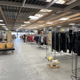Winkelvloer met kledingrekken, stellingen met spullen en decoratieve items in een ruime kringloopwinkel