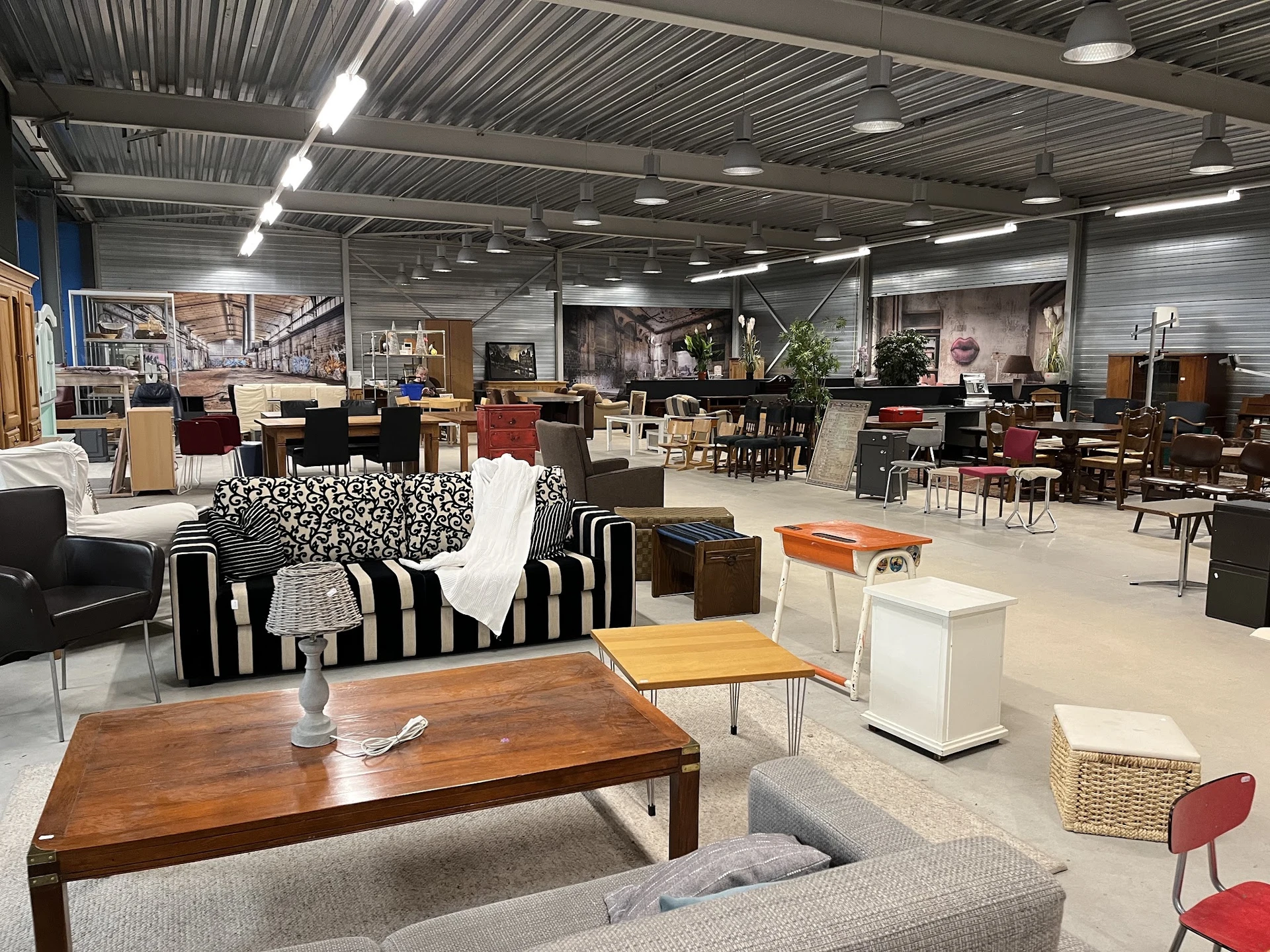 Ruime winkelhal met diverse meubels en huishoudartikelen uitgestald, met gestreepte bank, houten tafels en stoelen