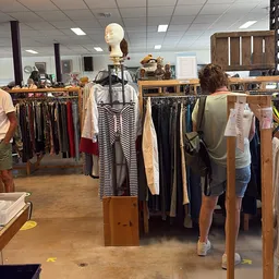 Rekken met tweedehands kleding, waaronder broeken, shirts en jurken in verschillende kleuren