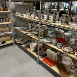 Stellingen met tweedehands serviesgoed, borden, kopjes en decoratieve items uitgestald