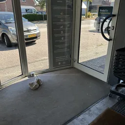 Ingang van een winkel met glazen deuren en uitzicht op parkeerplaats buiten