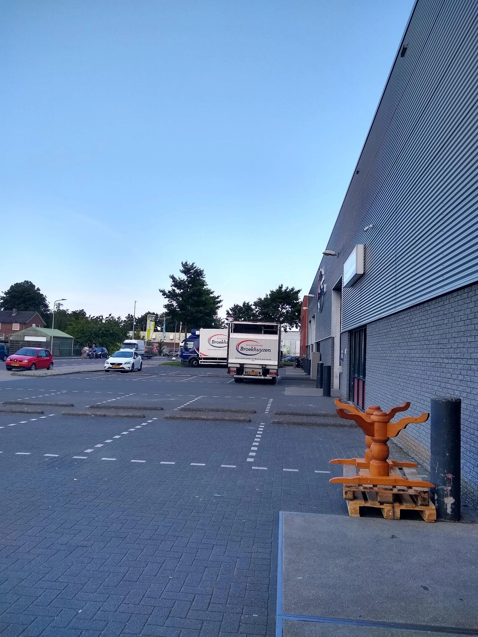 Parkeerterrein met bestelwagen en hoek van bakstenen gebouw, bomen op achtergrond