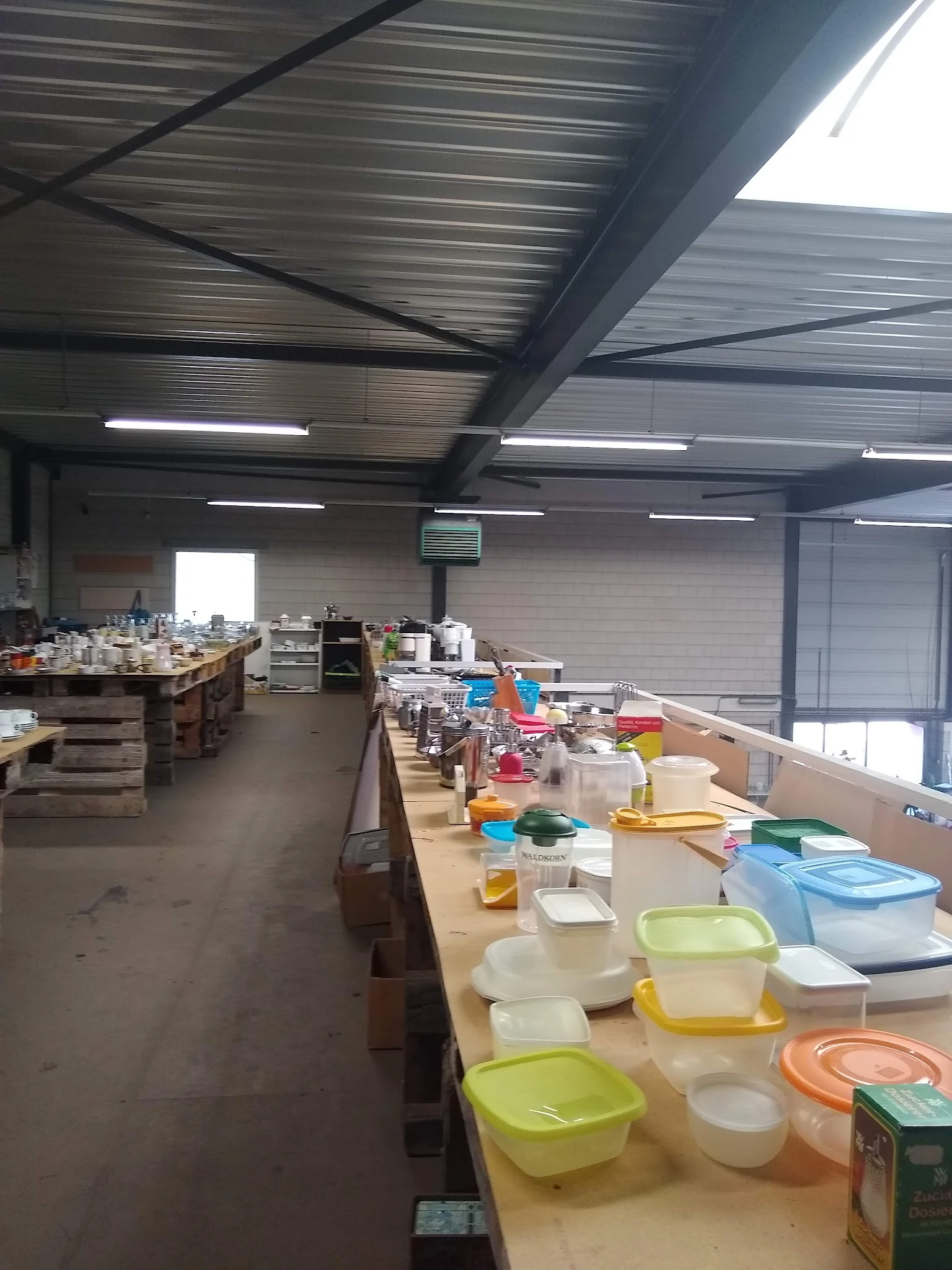 Magazijnruimte met lange werkafels vol met diverse huishoudelijke artikelen en opbergboxen