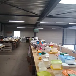 Magazijnruimte met lange werkafels vol met diverse huishoudelijke artikelen en opbergboxen