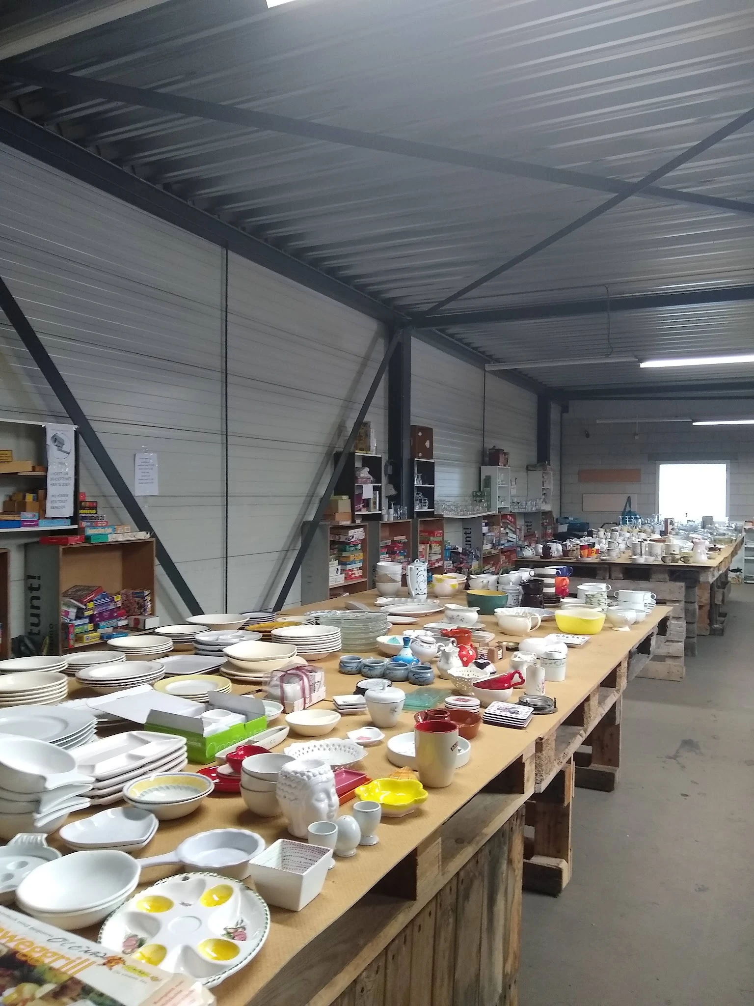 Tafel vol huishoudelijk servies, borden, schalen en ander gebruikt keramiek in een kringloopwinkel