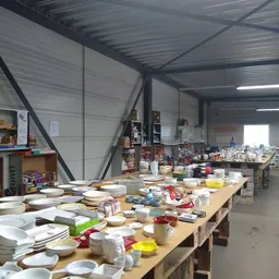 Tafel vol huishoudelijk servies, borden, schalen en ander gebruikt keramiek in een kringloopwinkel