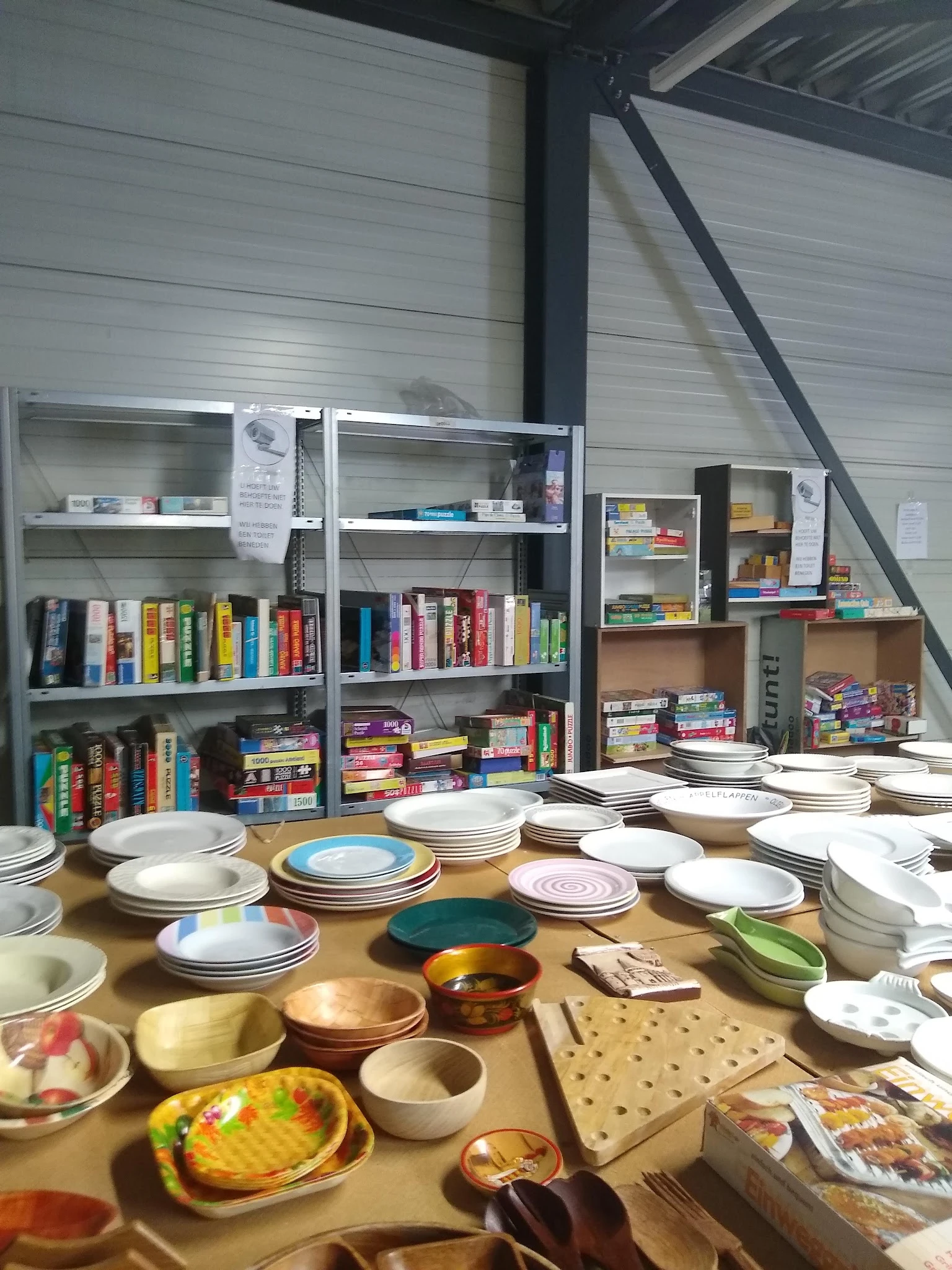 Tafels vol servies en borden in verschillende kleuren en stijlen, boekenkasten op achtergrond