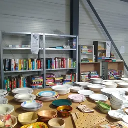 Tafels vol servies en borden in verschillende kleuren en stijlen, boekenkasten op achtergrond