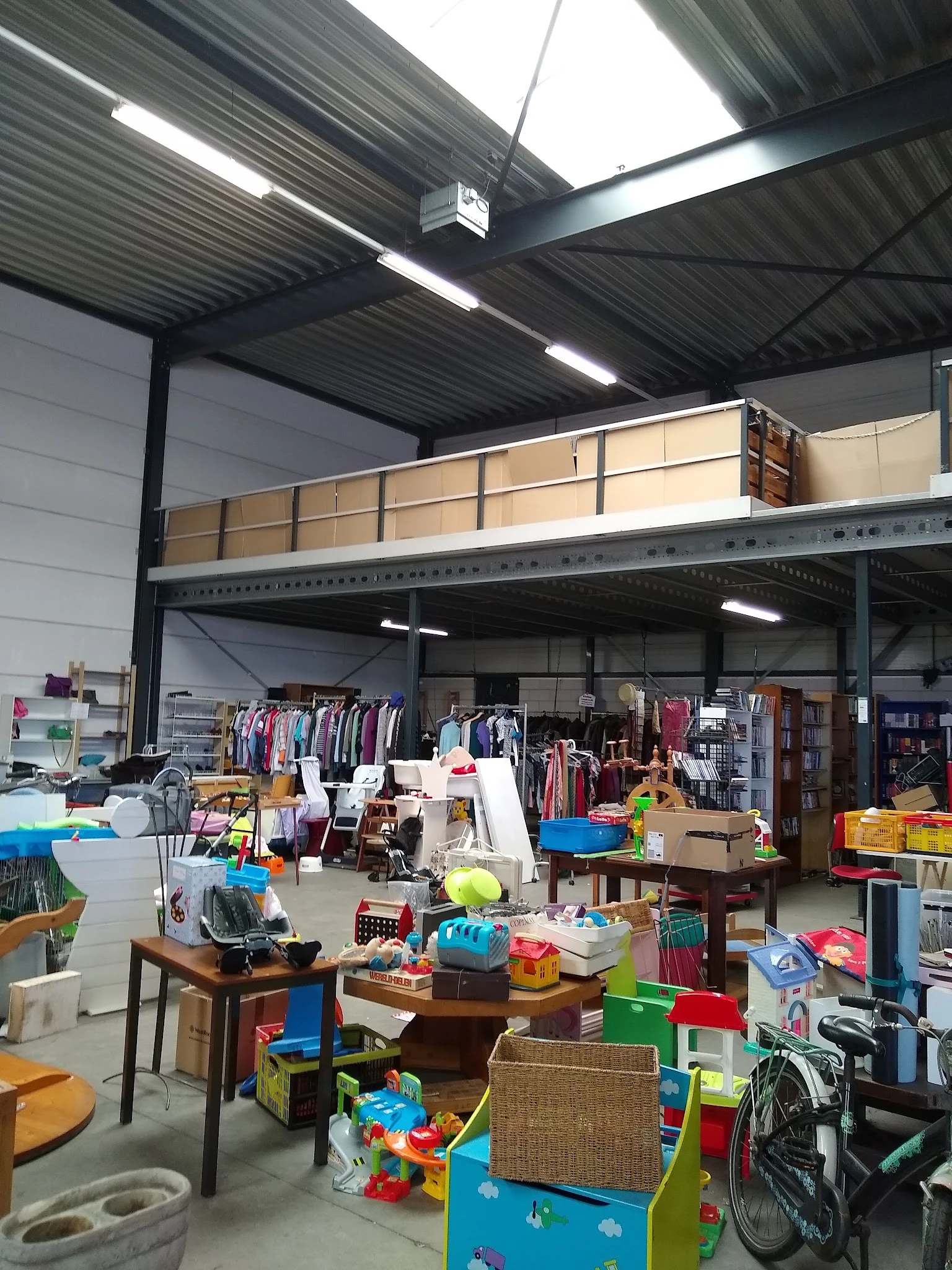 Overzicht van kringloopwinkel met kleding aan rekken, boekenkasten, speelgoed en huishoudelijke artikelen op tafels.