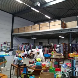 Overzicht van kringloopwinkel met kleding aan rekken, boekenkasten, speelgoed en huishoudelijke artikelen op tafels.