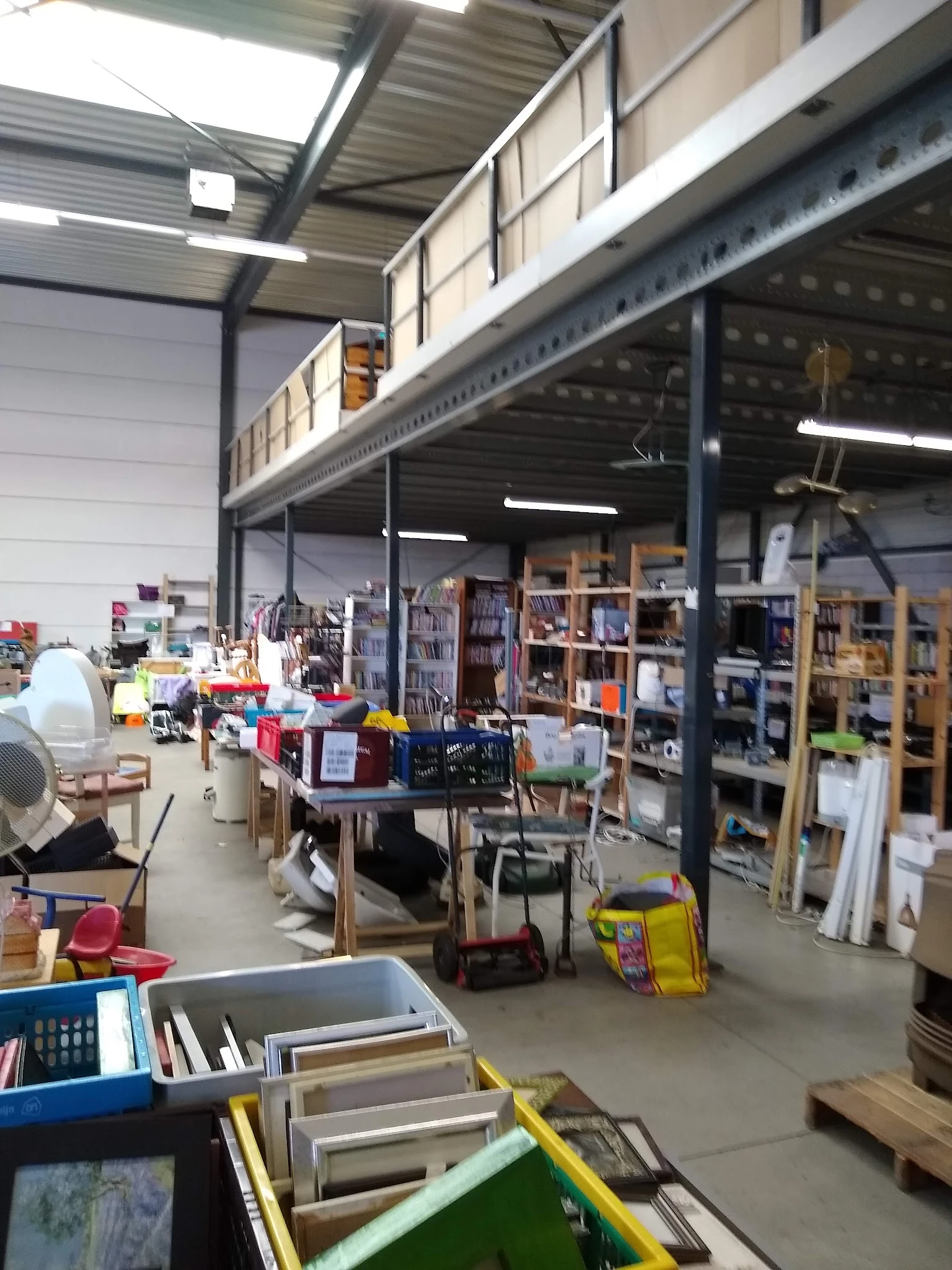 Overzicht van de winkelruimte met stellingen, boekenrekken, diverse spullen en gebruikte goederen verspreid door de hal