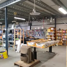 Ruim magazijn met boekenkasten, werkbank met materialen, bovenliggende LED-verlichting en diverse voorraad