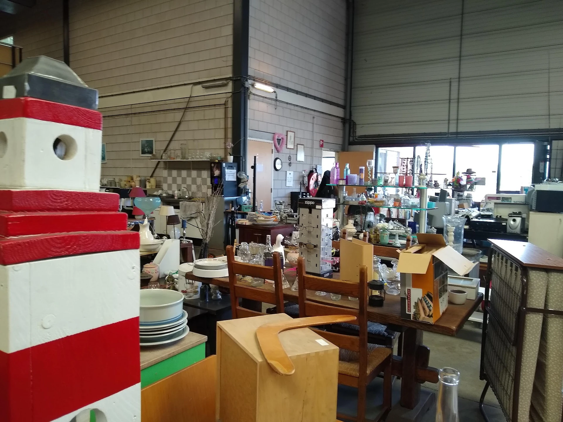 Overzicht van de winkelruimte met diverse gebruiksartikelen, meubels en huishoudspullen op tafels en stellingen.