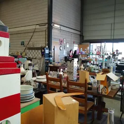 Overzicht van de winkelruimte met diverse gebruiksartikelen, meubels en huishoudspullen op tafels en stellingen.
