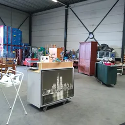 Magazijnruimte met diverse tweedehands meubels, stoelen, kasten en huishoudelijke spullen verspreid over de vloer