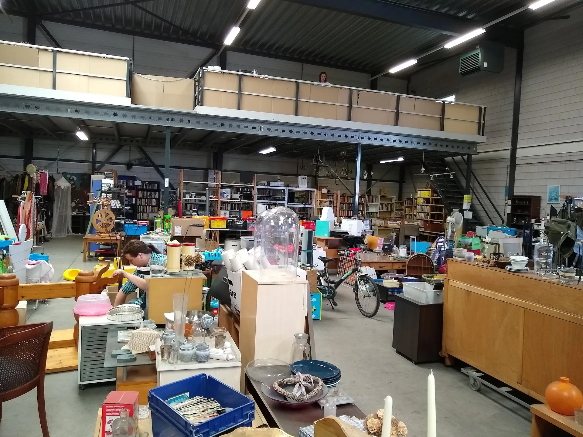 Overzicht van de kringloopwinkel met diverse spullen, meubels en artikelen door elkaar op de vloer en stellingen