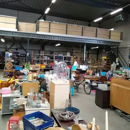 Overzicht van de kringloopwinkel met diverse spullen, meubels en artikelen door elkaar op de vloer en stellingen