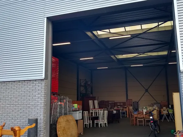 Ruime magazijnhal met houten meubels, stoelen en diverse voorwerpen uitgestald tegen de wanden