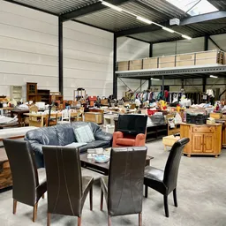 Ruim magazijn met diverse tweedehands meubels, stoelen, tafels en huishoudartikelen uitgestald op de vloer