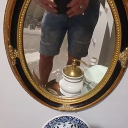 Spiegelafbeelding van persoon in spijkerbroek met witte pot met gouden deksel op tafel