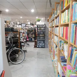 Winkelinterieur met houten boekenkasten vol gekleurde boeken, fiets links, en diverse stellingen met tweedehands artikelen