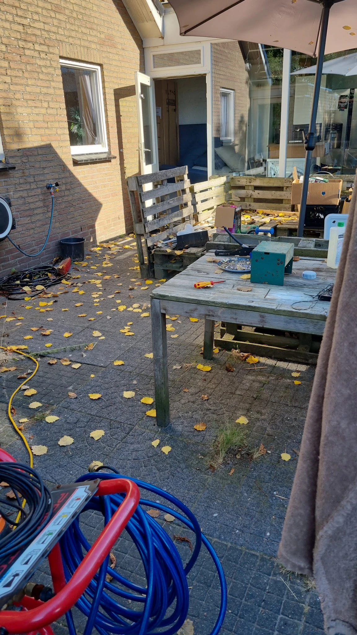 Buitenruimte/terras met werkbank en uitgestalde spullen, bladeren op de grond