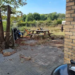 Picknickplaats met tafel, fiets en bakstenen gebouw aan de rand van een terrein