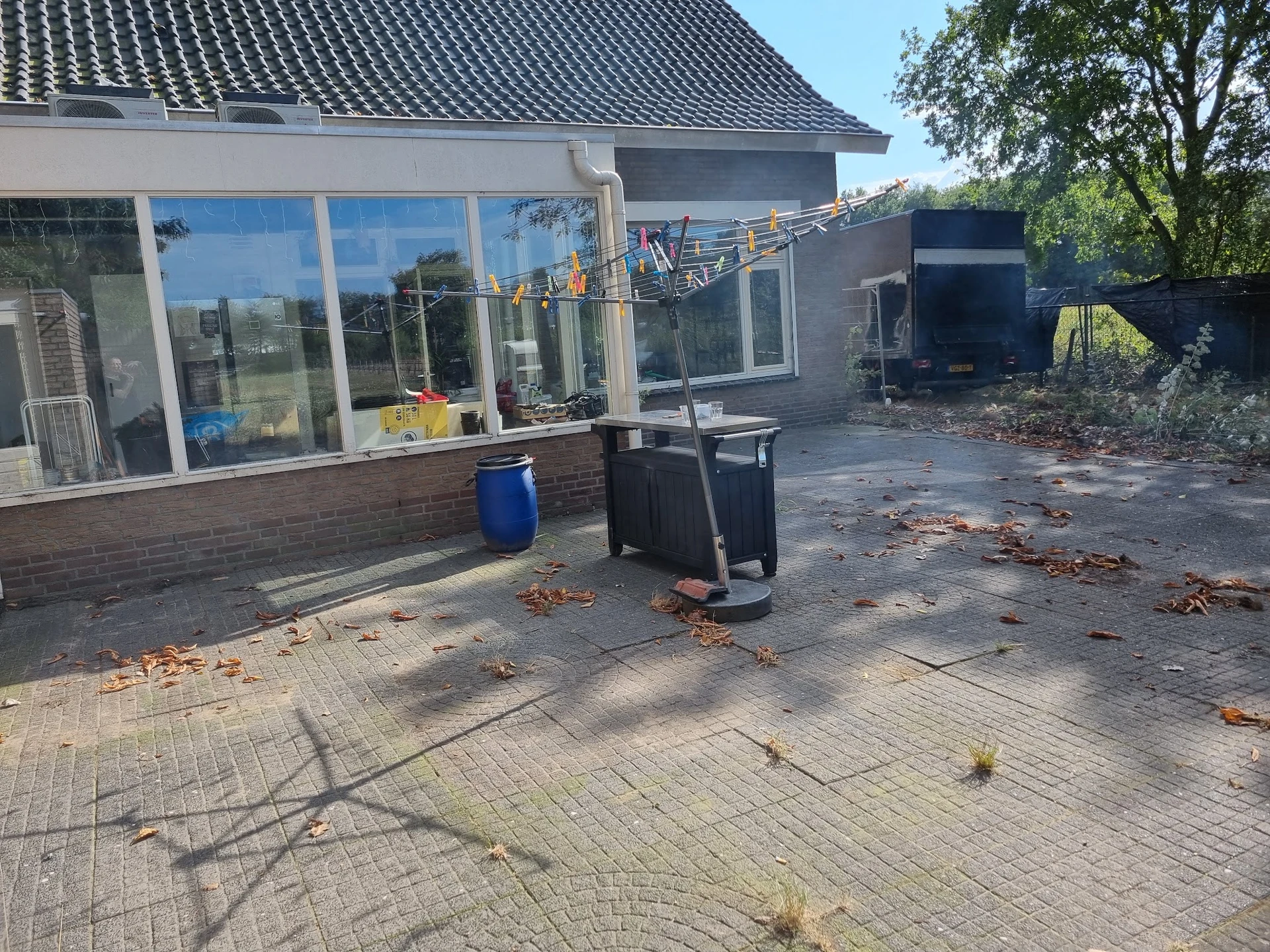 Buitenkant van kringloopwinkel met grote ramen, blauwe ton en zwarte containers op geplaveid terras