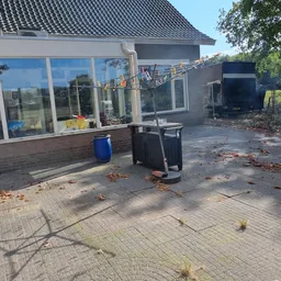 Buitenkant van kringloopwinkel met grote ramen, blauwe ton en zwarte containers op geplaveid terras