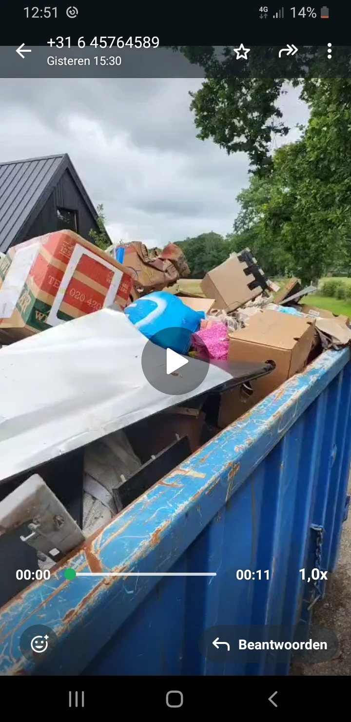 Blauwe container vol met kartonnen dozen en huishoudelijke spullen bij een kringloopwinkel