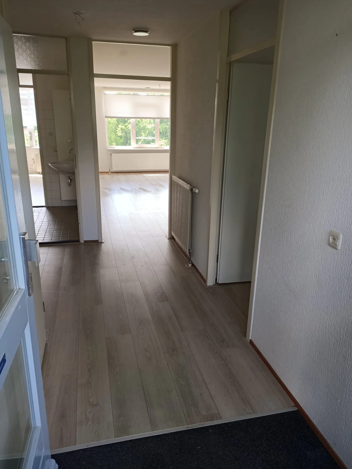 Lege winkelgang met donkere houten vloer, witte wanden en deuren aan beide zijden