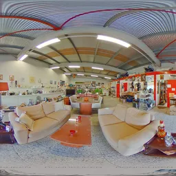 Ruim interieur van kringloopwinkel met beige banken, oranje tafels en rode kasten, stellingen met spullen langs de wanden