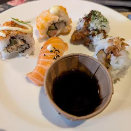 Bord met vier verschillende sushi rollen en een kommetje sojasaus